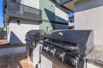 A stainless steel grill with four burners is on a patio.